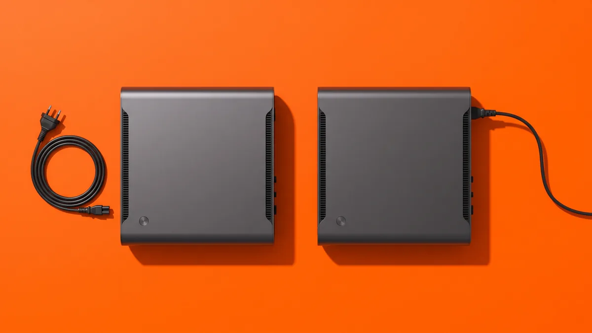 Zwei baugleiche kompakte Mini-PCs nebeneinander von oben auf orangem Grund — beim linken liegt das abgezogene Stromkabel aufgerollt daneben, der rechte ist angeschlossen und startklar