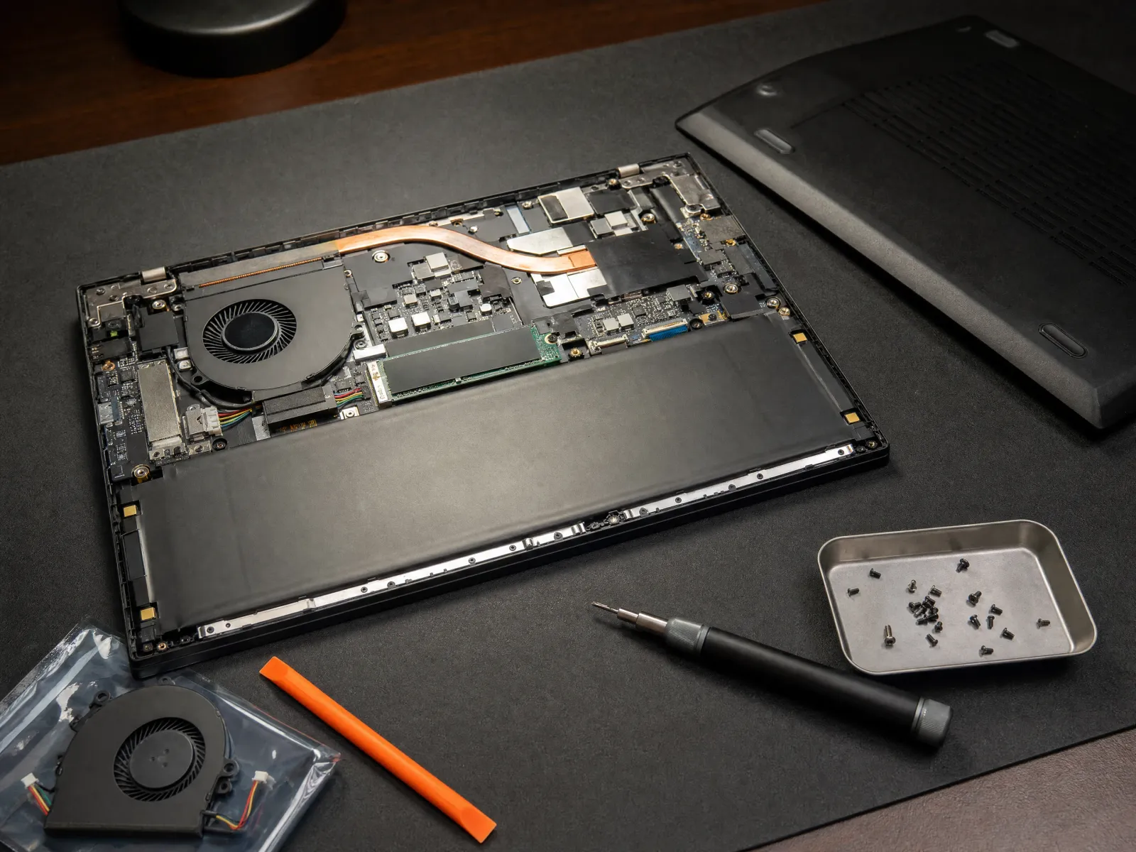 Laptop-Reparatur: geöffneter Laptop mit sichtbarem Innenleben, sortierte Schrauben und Ersatzlüfter auf der Werkbank